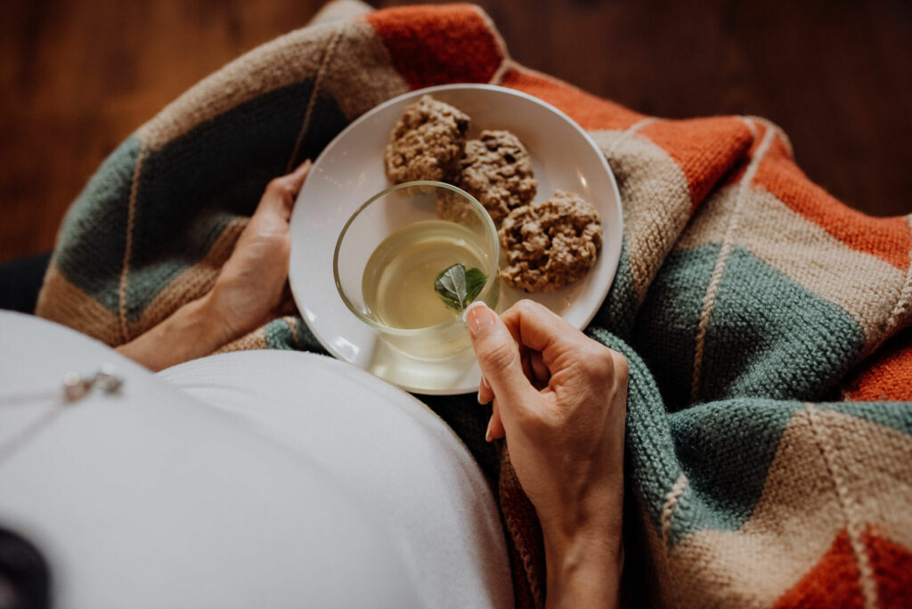A person holding a white plate with cookies and a drink on it.