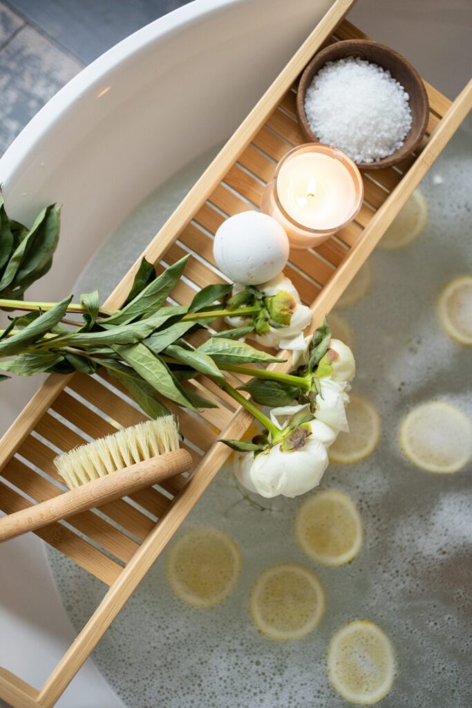 A bathtub with a bath shelf over top of it with bath salts, roses, a candle, and a scrub brush on top.
